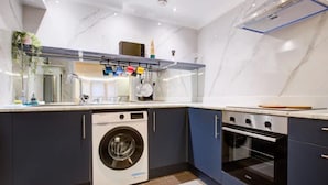 A modern kitchen with a built-in washer and oven, dark cabinetry, and a marble backsplash. - Stunning London City Apartment Retreat (London)