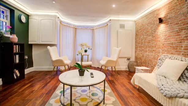 A cozy living room with a round coffee table, two white armchairs, a white sofa, and a brick accent wall. - Stunning London City Apartment Retreat (London)