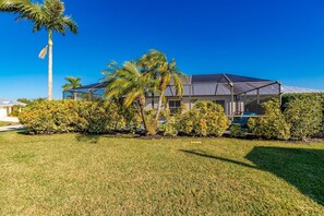 A two-story house with a covered patio, surrounded by well-maintained grass and various shrubs.