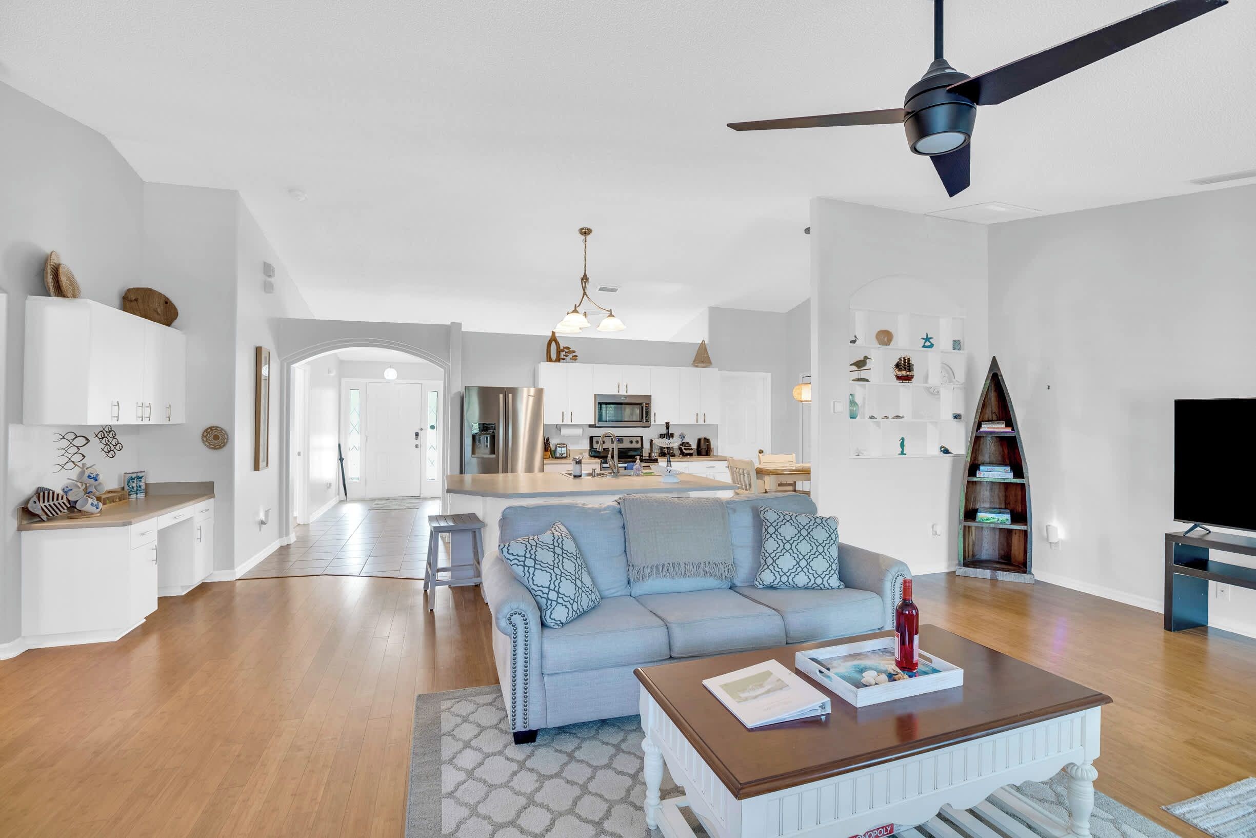 A modern living room with a sofa, coffee table, and a TV. There is a kitchen in the background with a dining area.