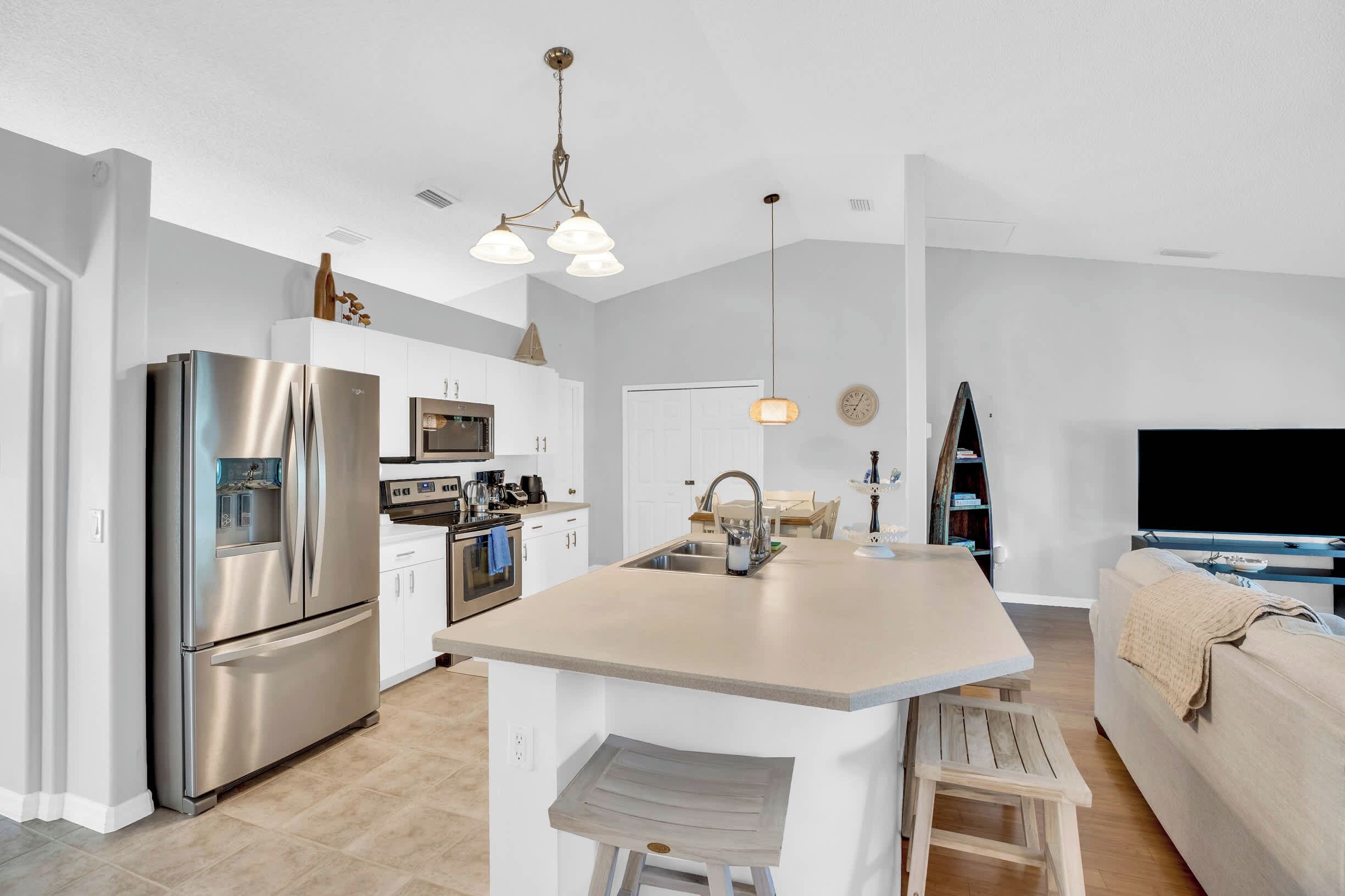 A modern kitchen with a central island, stainless steel appliances, and a dining area with a sofa and TV.