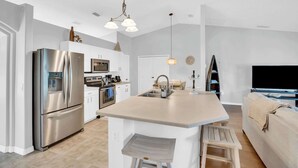 Una cucina moderna con isola centrale, elettrodomestici in acciaio inossidabile e zona pranzo con divano e TV.