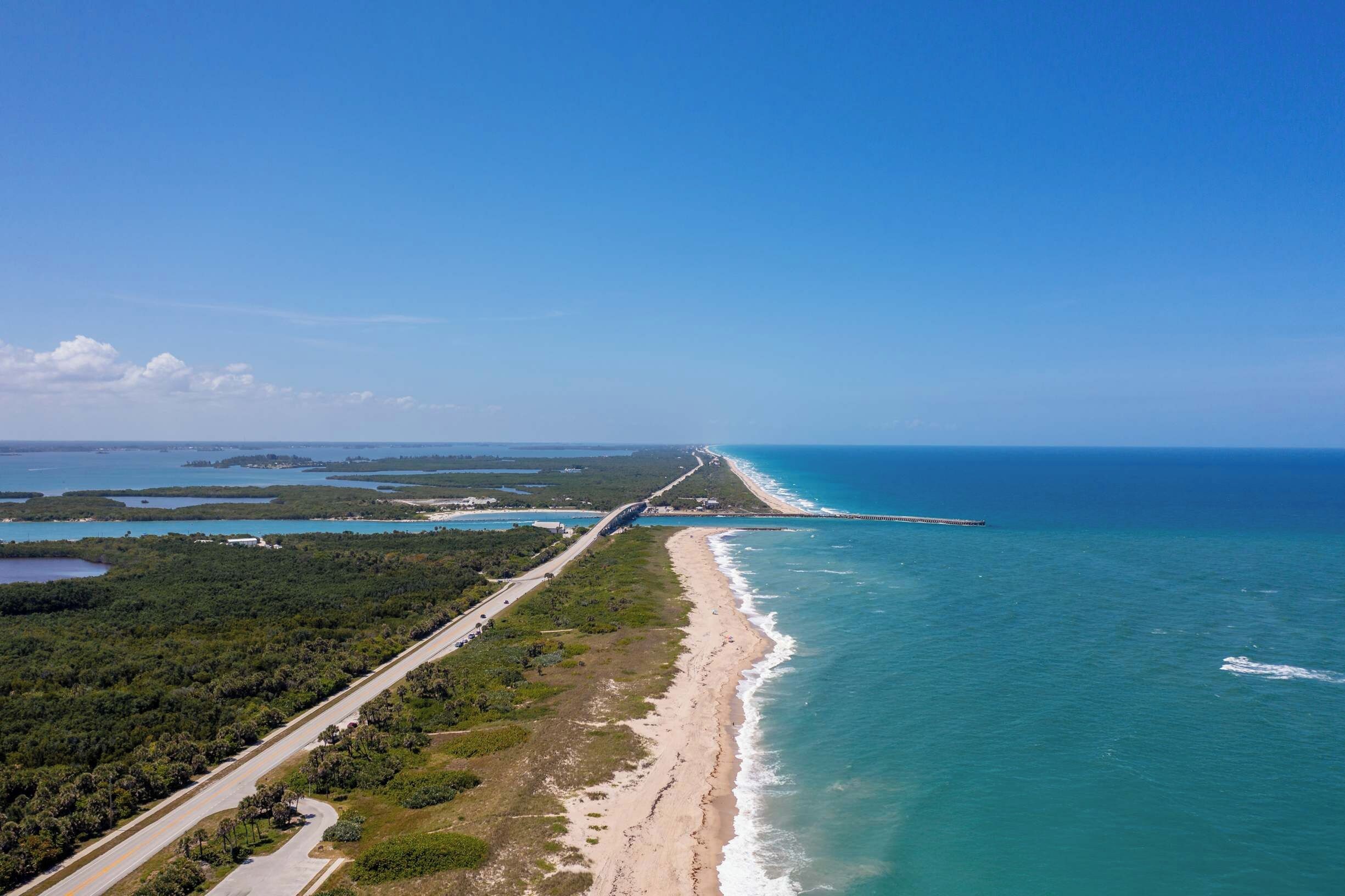 An aerial view of a coastal road with a beach and a bridge.