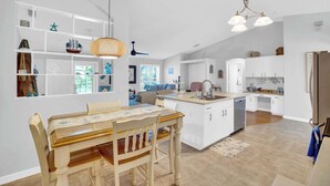 Una cucina moderna con mobili bianchi, un'isola centrale e un'area pranzo con tavolo e sedie in legno.