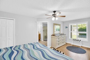 A bedroom with a bed, dresser, ceiling fan, and a window with blinds.