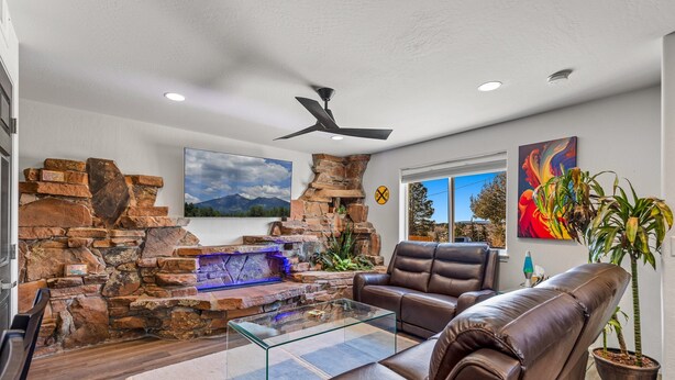 A living room with a stone fireplace, leather sofa, glass coffee table, and a mounted TV. - Terrace Main | 5BR/3BA  | Spend Spring in Flagstaff! (Flagstaff)