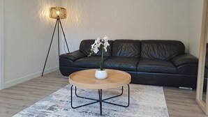A living room with a black leather sofa, a round wooden coffee table with a white vase, and a floor lamp. - Tainui Charm - Fully renovated, 2 bedrooms (Dunedin)