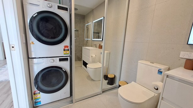Ein kleines Badezimmer mit Waschmaschine, Toilette und Duschkabine aus Glas.