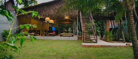 A thatched-roof structure with outdoor seating and a staircase leading to a higher level.
