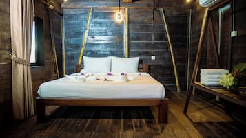 A wooden-framed bed with white linens and decorative swans, a wooden floor, and a rustic wall with a window and an air conditioning unit.