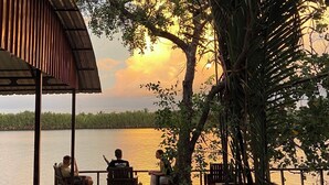 A wooden pavilion with benches and tables overlooking a calm body of water, surrounded by trees and vegetation.