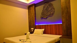Una cama bien hecha con una manta y almohadas blancas, una mesita de noche con lámpara, y un adorno decorativo sobre la cama.