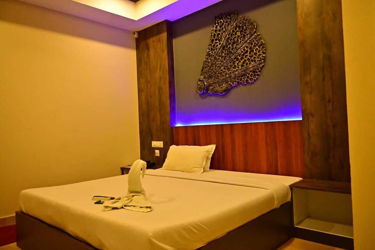 Una cama bien hecha con una manta y almohadas blancas, una mesita de noche con lámpara, y un adorno decorativo sobre la cama.