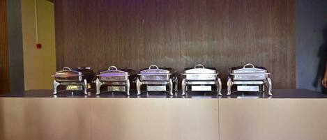 A buffet setup with five silver chafing dishes on a counter.