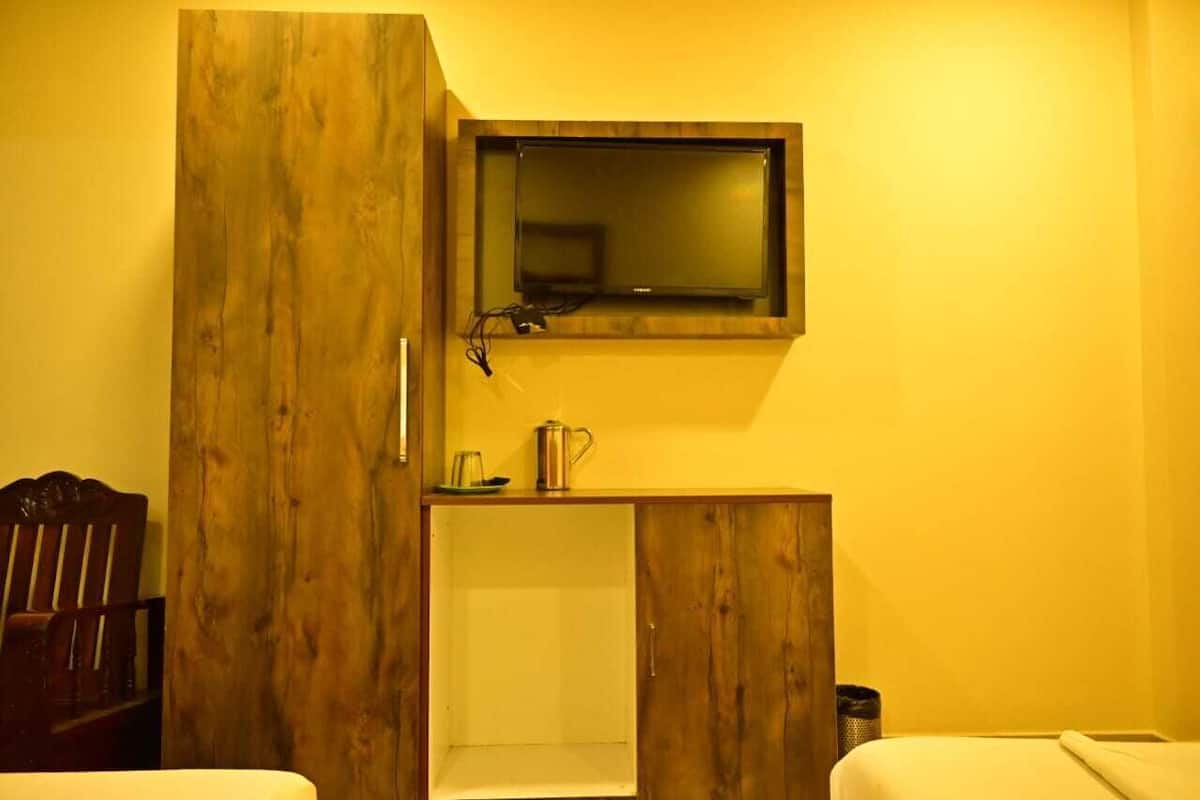 Una habitación compacta con un armario de madera, una mesita con un hervidor y un televisor colocado encima.