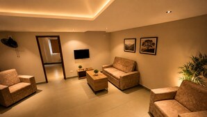 A modern living room with sofas, a coffee table, and a flat-screen TV. - Hypolux Business Hotel (Palakkad)