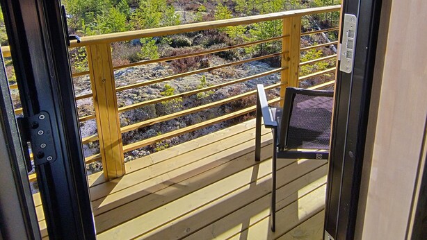 A wooden deck with a view of a mountainous landscape, a chair, and a railing.