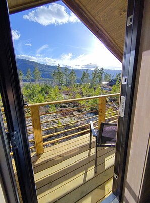 A wooden deck with a view of a mountainous landscape, a chair, and a railing.