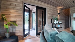 A modern log cabin interior with a grey sofa, a potted plant, and a bookshelf.