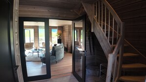 A modern interior with a wooden staircase, a living area with a sofa and coffee table, and a view of the outdoors.