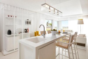 Una cocina moderna con una isla central, muebles blancos y vistas al exterior.