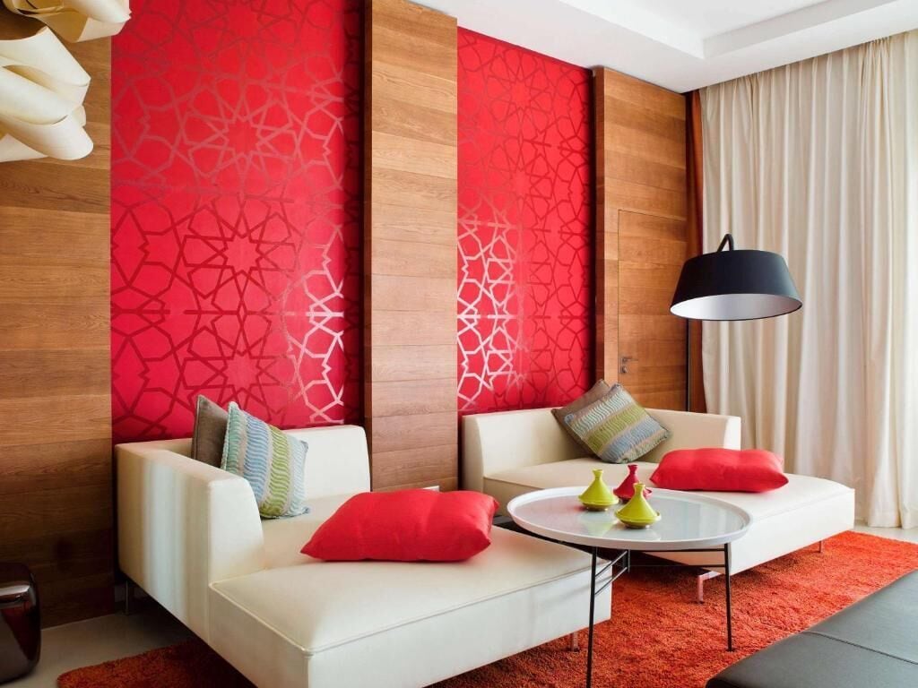 A modern hotel room with two white sofas, a round coffee table, and a red patterned wall.