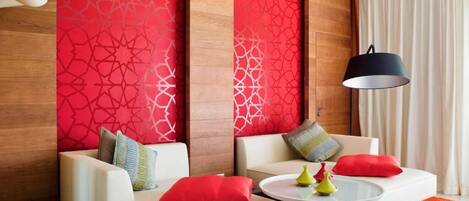 Una habitación de hotel moderna con dos sofás blancos, una mesa redonda de centro y una pared con estampado rojo.