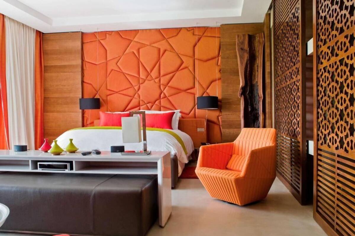 A modern hotel room with a large bed, a sofa, a chair, and a decorative wall.