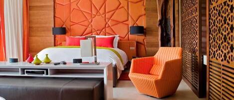 A modern hotel room with a large bed, a sofa, a chair, and a decorative wall.
