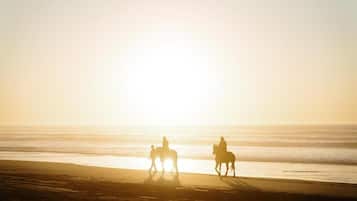 A beach scene with three people riding horses.