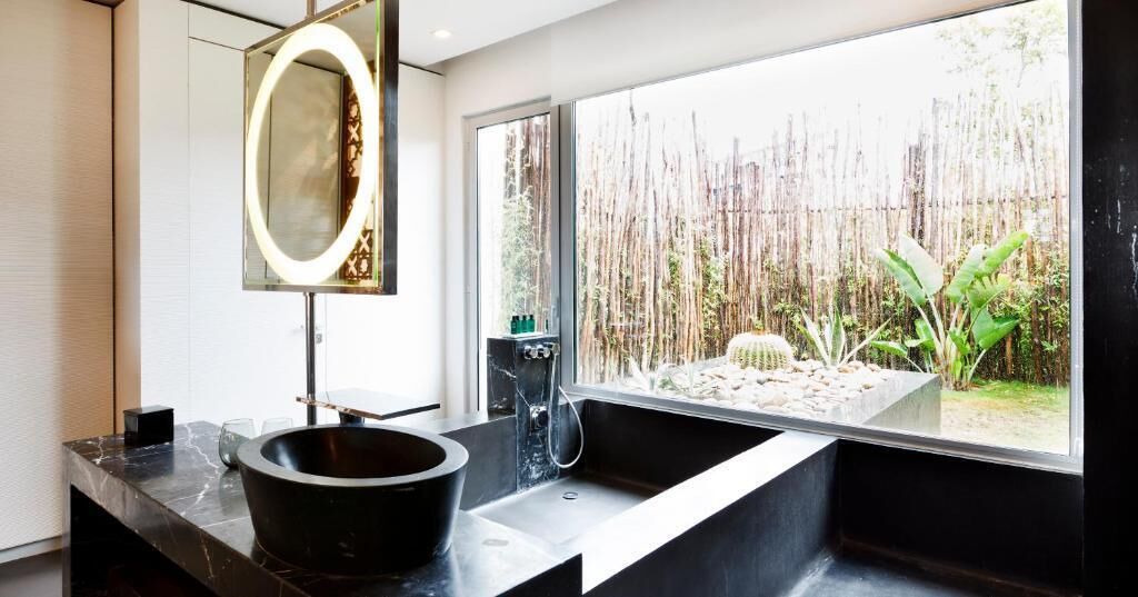 Ein modernes Badezimmer mit großem Fenster, einem schwarzen Waschbecken und einem beleuchteten Spiegel.