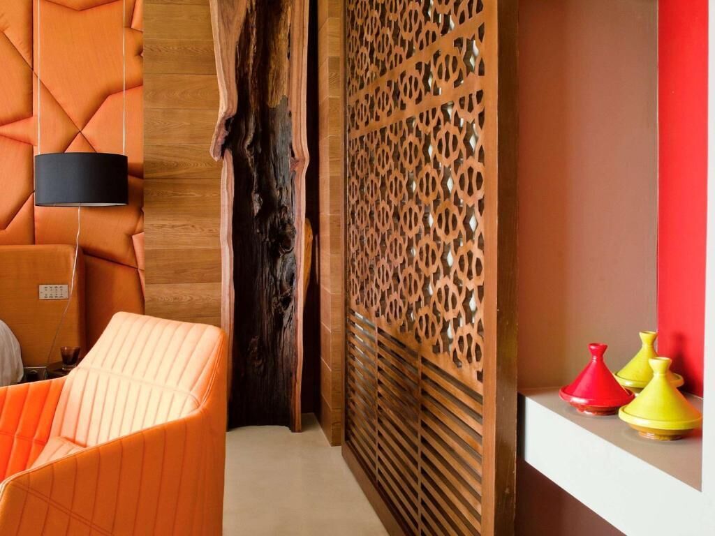 Una habitación con un separador de madera, una butaca acolchada, un televisor de pantalla plana y una estantería con jarrones decorativos.