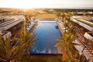 Piscina infinita en la azotea con vistas despejadas del paisaje, rodeada de sillones de descanso y palmeras.