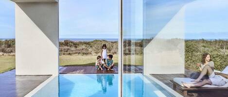 Un espace piscine extérieur moderne doté de parois en verre, offrant une vue dégagée sur le paysage, et d’une terrasse en bois.