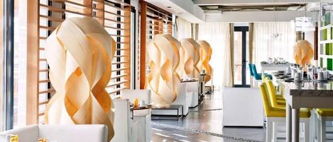 Un hall d’hôtel moderne au design épuré, avec un long comptoir d’accueil, des canapés blancs et un mur décoratif central.