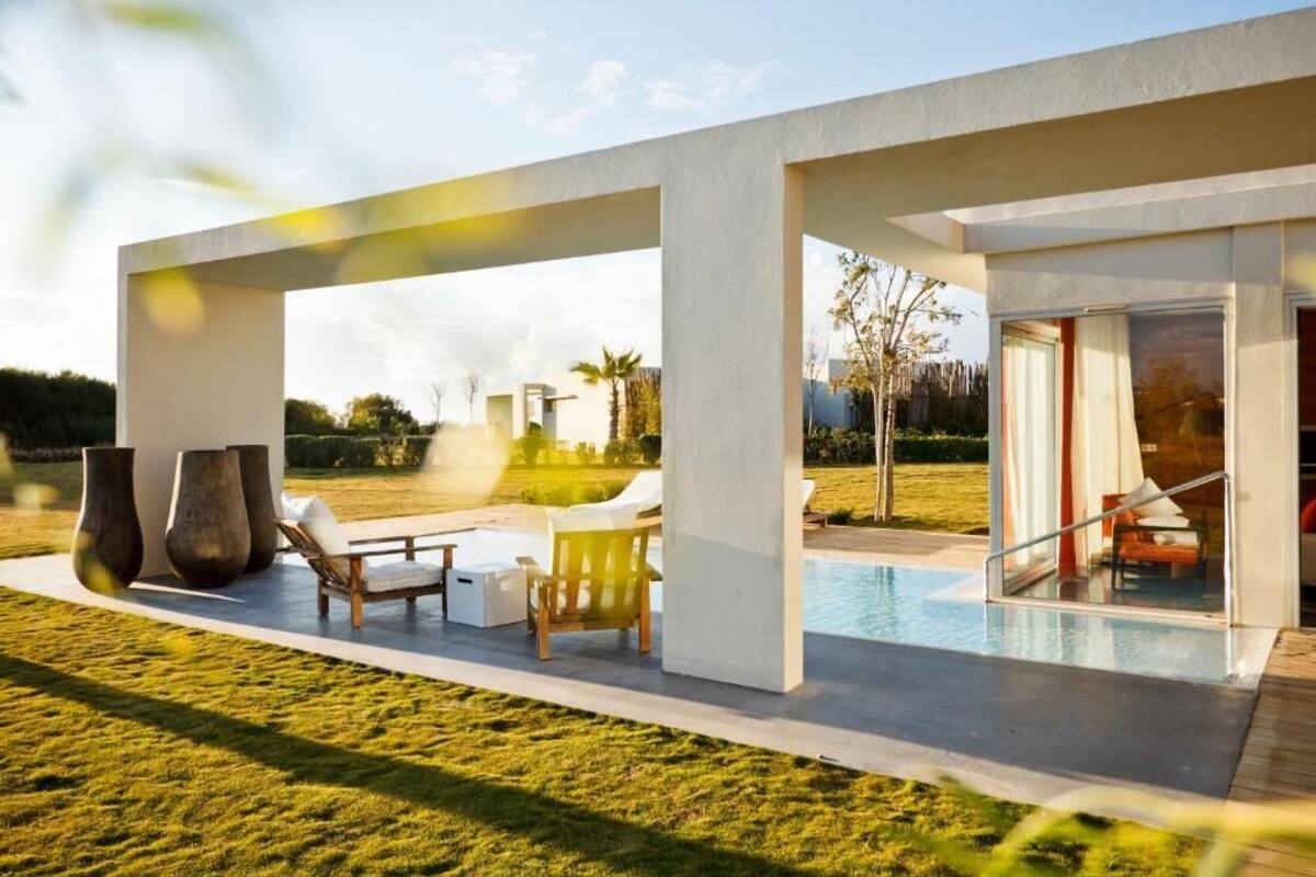 A modern outdoor pool area with lounge chairs and a table, surrounded by a well-maintained lawn and a clear sky.