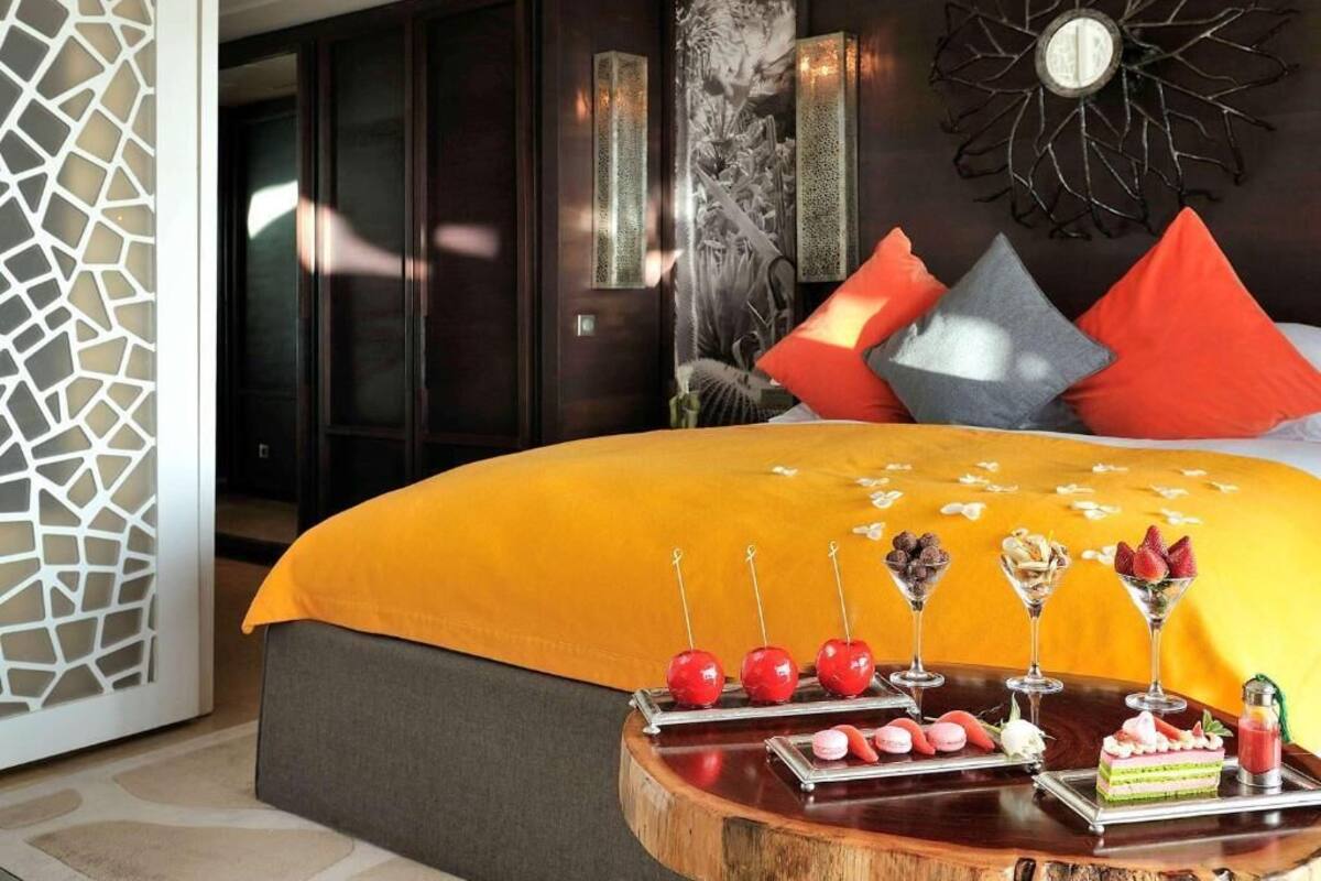 A hotel room with a large bed, a wooden side table with snacks, and a decorative wall piece.