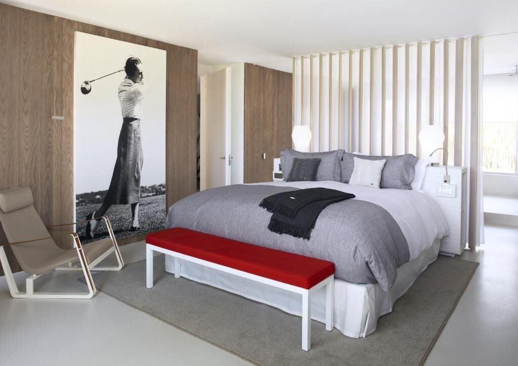Een moderne slaapkamer met een groot bed, een bankje, een stoel en een kunstwerk aan de muur.