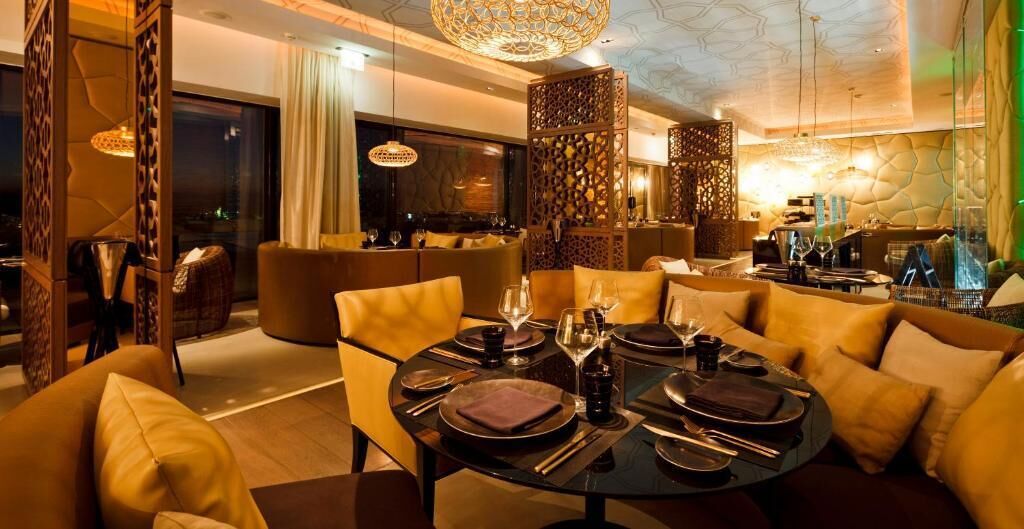 A modern dining area with round tables set for four, surrounded by plush sofas and a decorative partition.