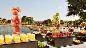 Une table de buffet proposant une variété de fruits, de jus et de desserts, le tout disposé devant un cadre extérieur pittoresque.
