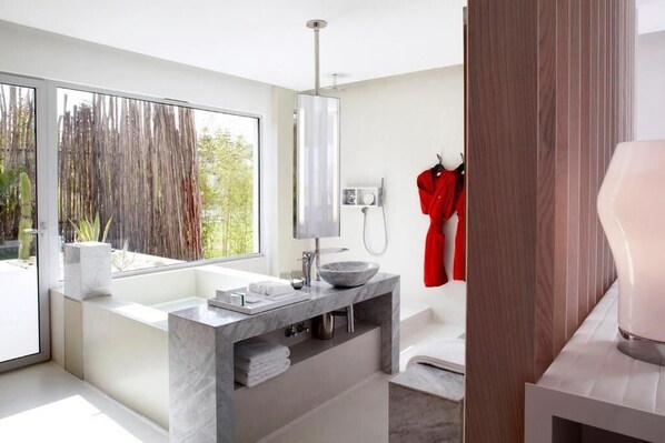 Un baño moderno con un ventanal grande, un lavabo de mármol y una bata roja colgada en la pared.