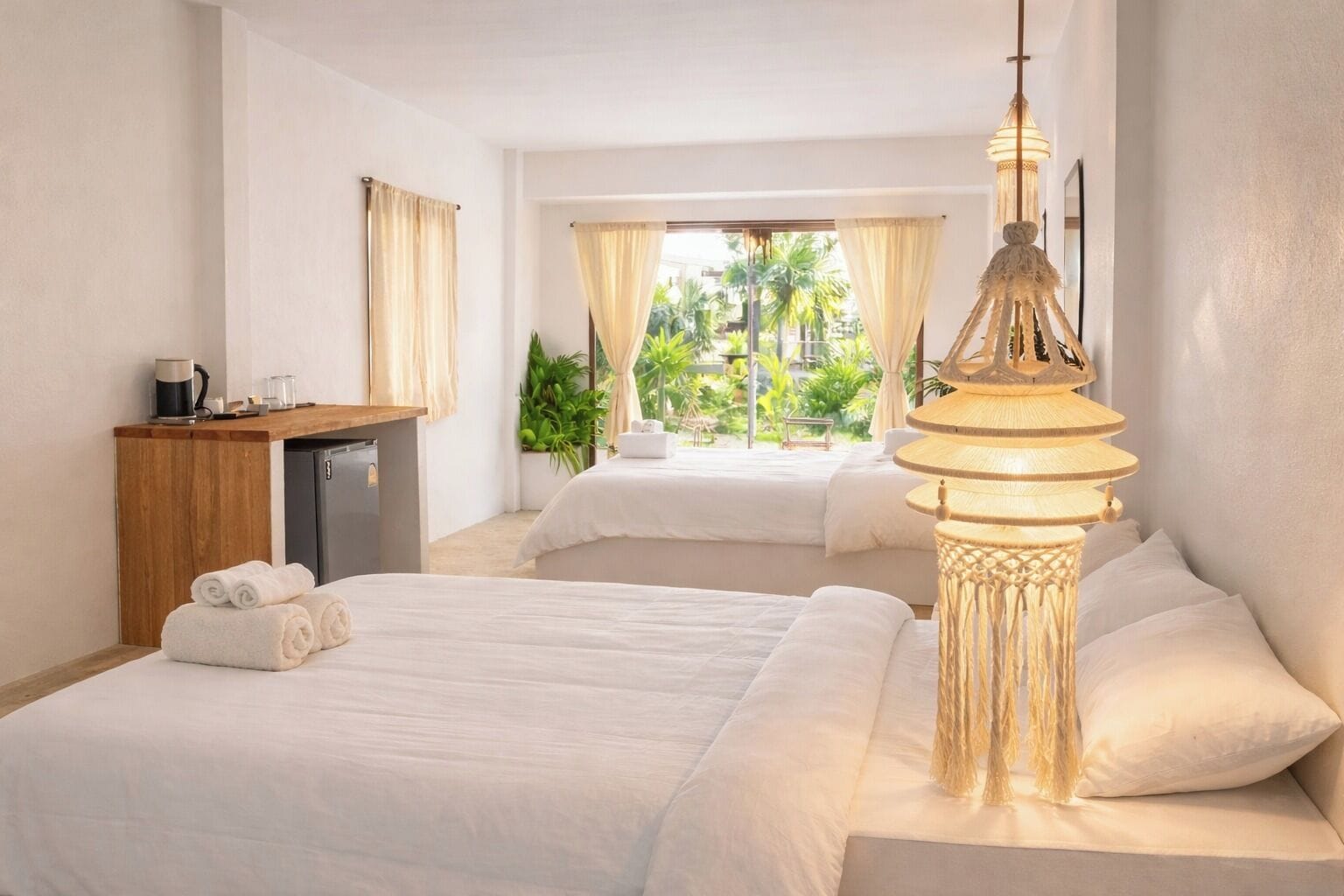 Ein Hotelzimmer mit zwei Betten, einem Schreibtisch, einer Lampe und Blick auf Grünflächen.