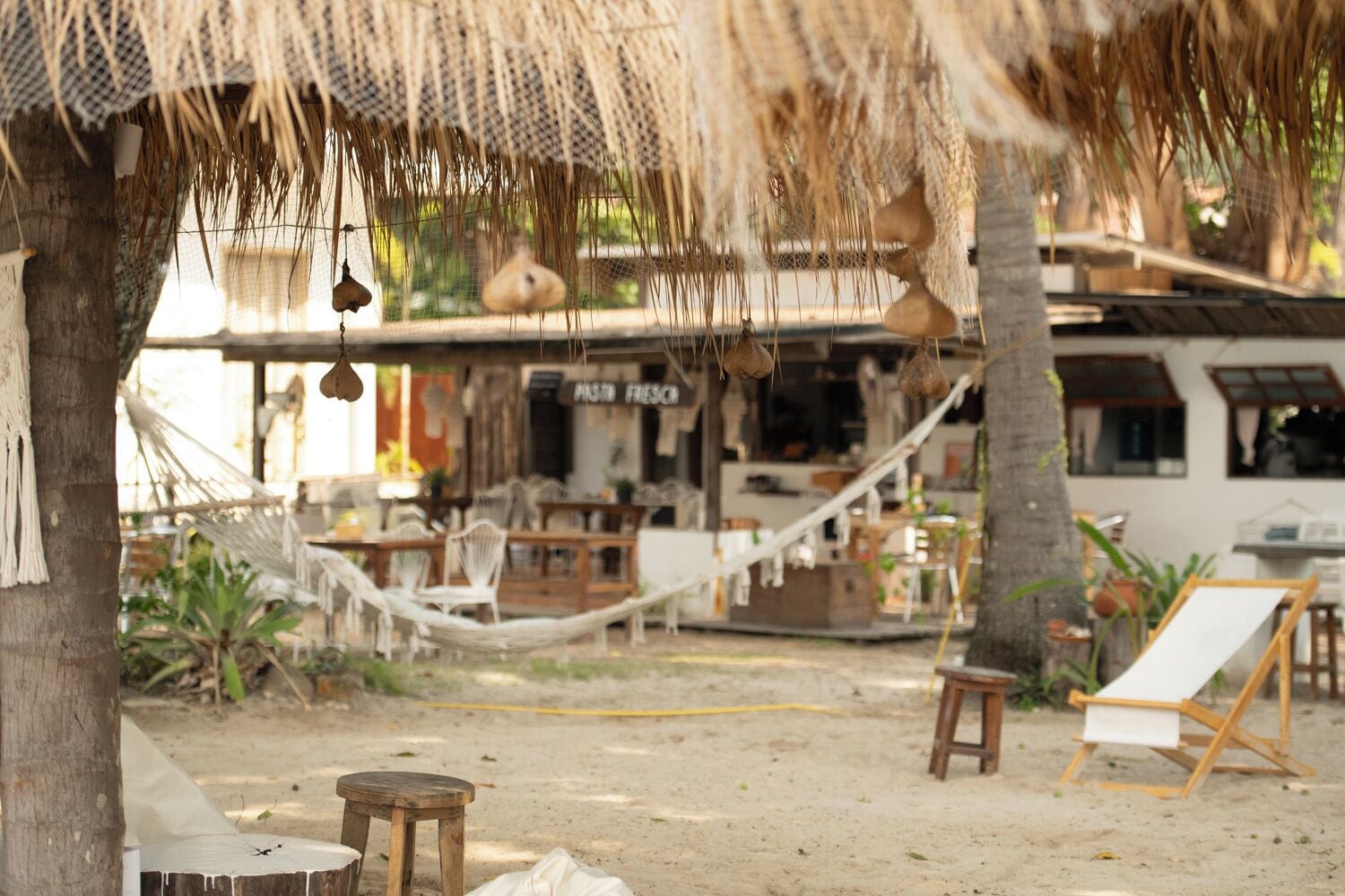 A beachside café with outdoor seating, including a hammock and lounge chairs, and a visible menu board.