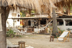 Un café frente a la playa con terraza, incluyendo una hamaca y sillones de descanso, y un cartel de menú visible.