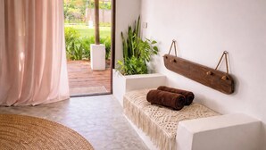 A room with a view of a garden, a wooden wall-mounted shelf with towels, a woven bench, and a large window with curtains. - Riva Boutique Resort Koh Chang (Ko Chang)