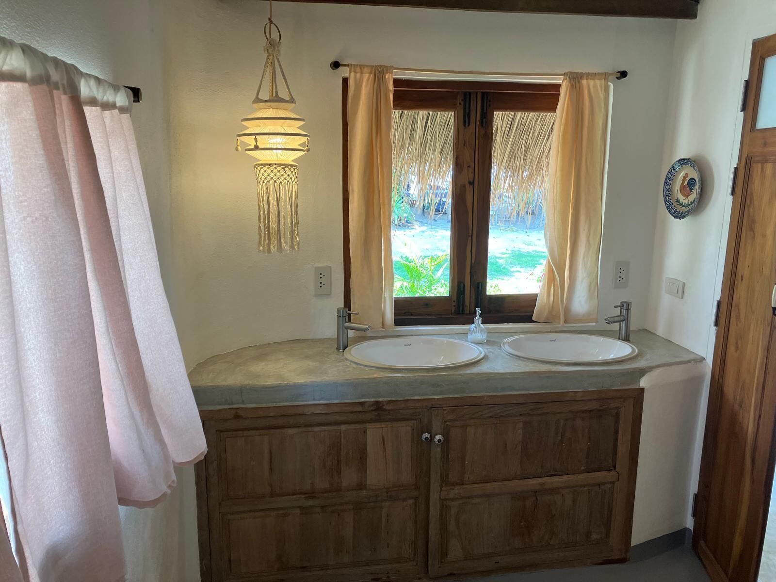 A bathroom with two sinks, wooden cabinets, a hanging light fixture, and a view of greenery outside.
