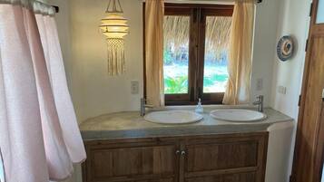 A bathroom with two sinks, wooden cabinets, a hanging light fixture, and a view of greenery outside.