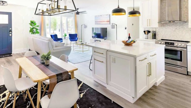 Een moderne keuken met witte kasten, een centraal eiland, roestvrijstalen apparatuur en hangende lampen.