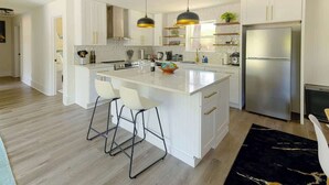 Een moderne keuken met witte kasten, een centraal eiland met barstoelen, een roestvrijstalen koelkast en hanglampen.