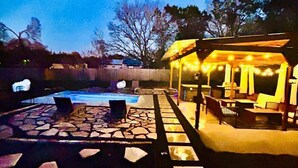 Een terras met een zwembad, buitenmeubels en een overdekt gedeelte met lichtjes.